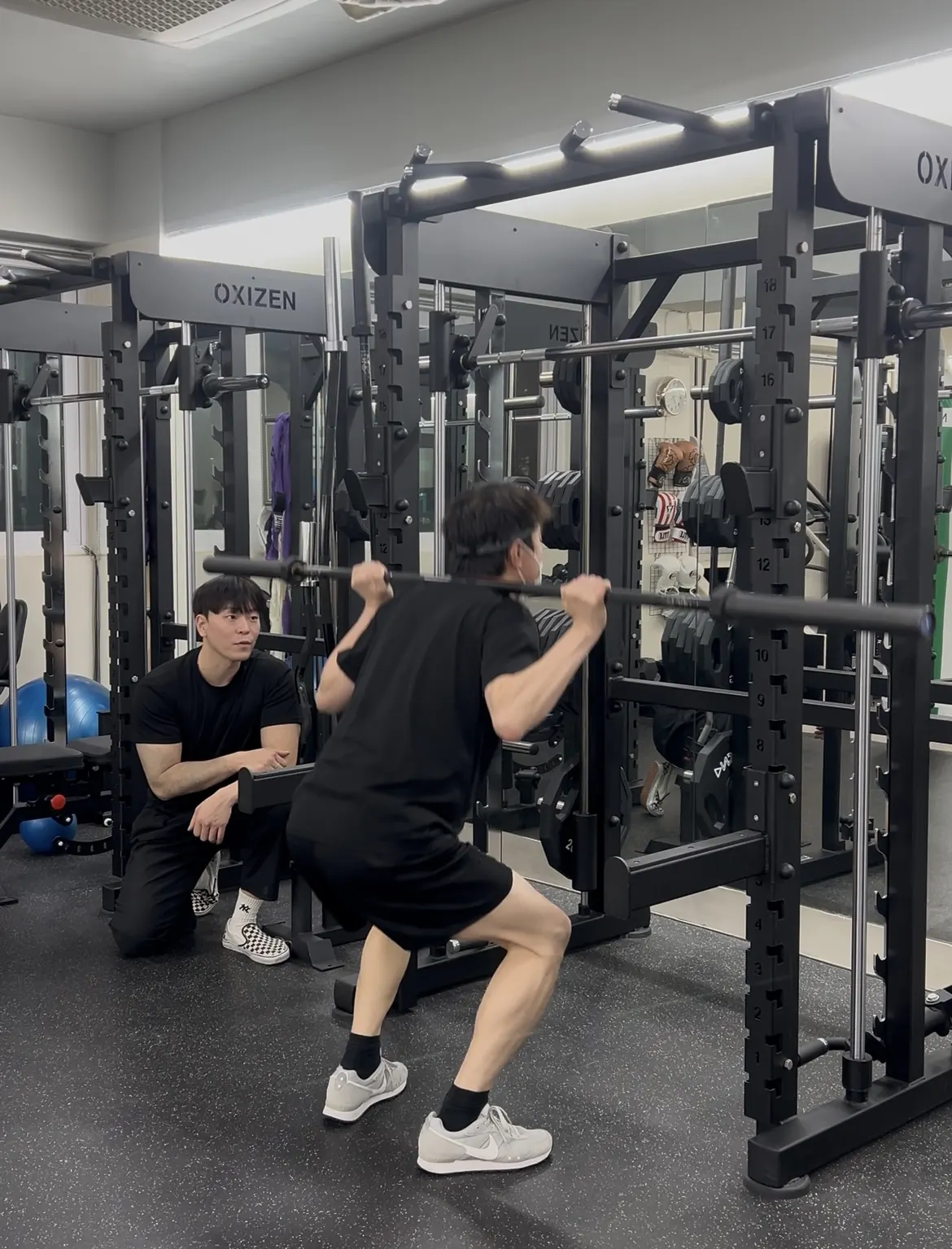 Coach Kang Jaehyun watching and correcting a member's squat form during a private PT session in Seoul